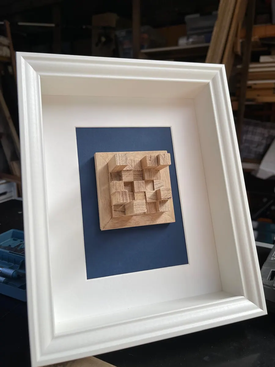 Three dimensional laser cut timber cube relief artwork mounted on navy card in a white box frame