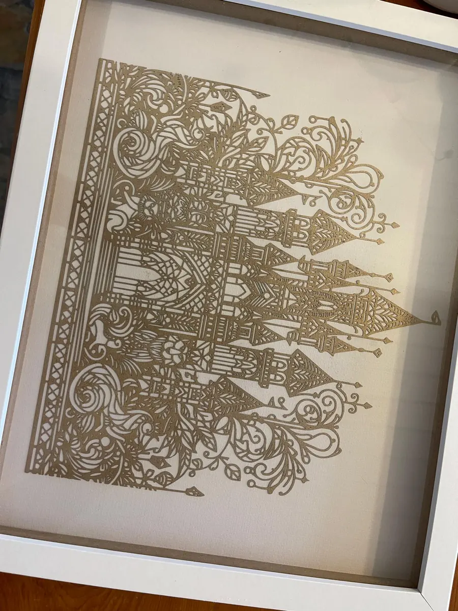 Intricate gold filigree laser cut panel with ornate scrollwork and spires, framed in white