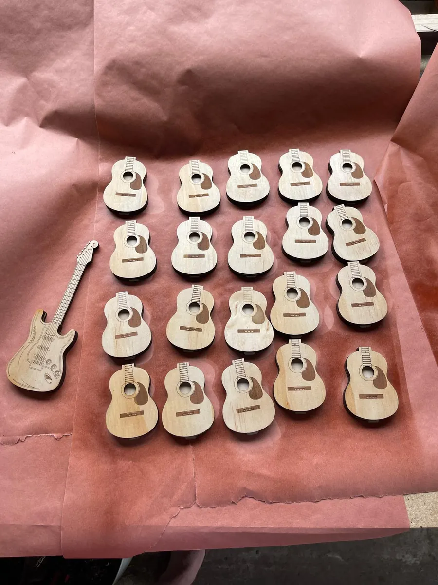 A batch of twenty identical laser cut timber guitar pieces laid out on packing paper after a production run