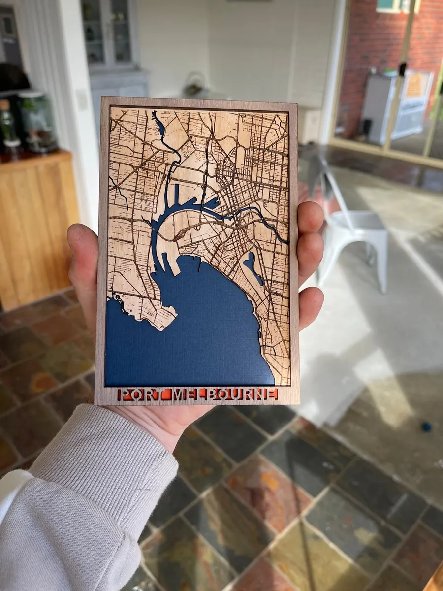 A small laser cut map of Port Melbourne held in a hand, showing the layered timber and blue water detail