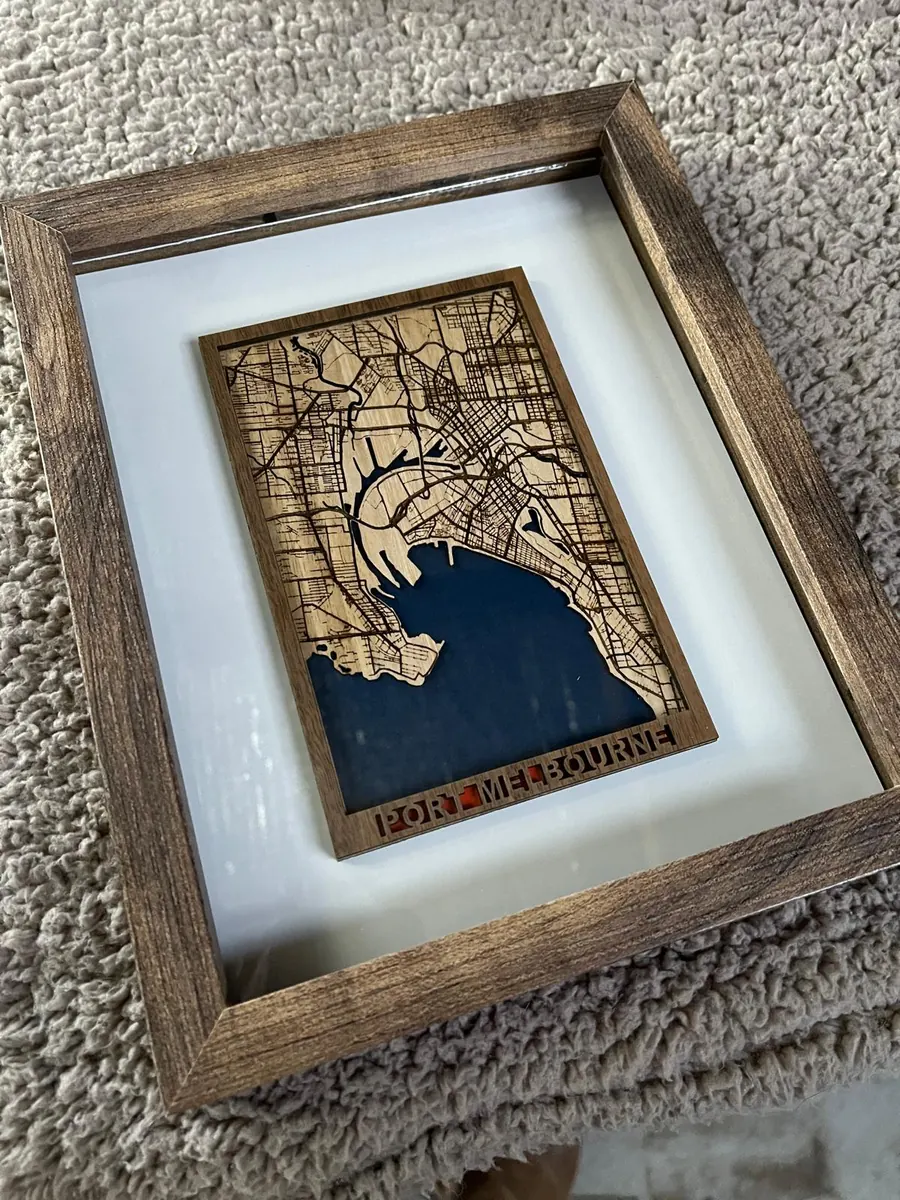 Laser cut map of Port Melbourne in walnut and pale plywood with blue water and cut-through lettering, in a shadow box frame
