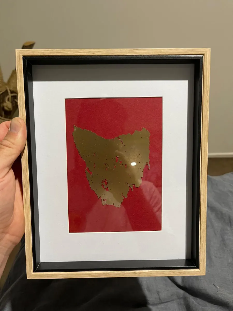 Framed laser cut silhouette map of Tasmania in a brushed gold finish mounted on deep red card in a shadow box