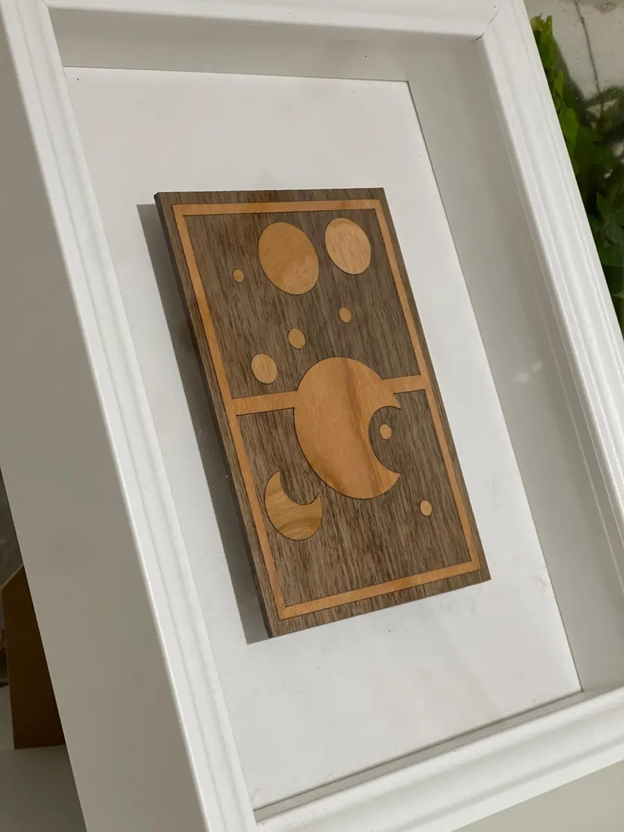 Laser cut moon phases wall art with pale timber inlaid into dark walnut, in a white shadow box frame