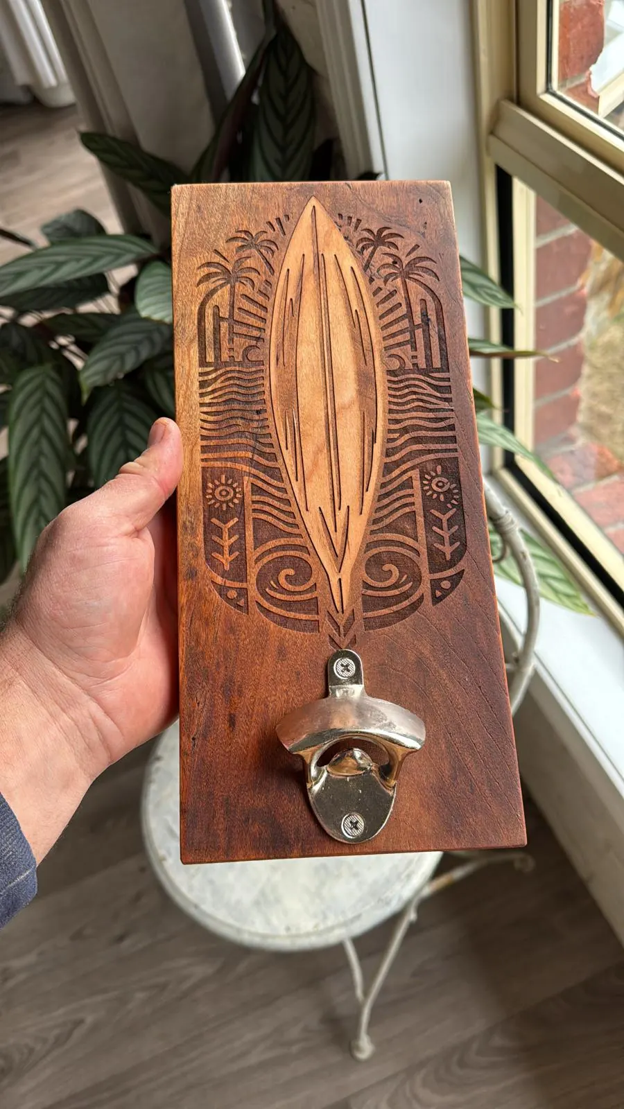 Wall mounted bottle opener on a stained timber board with a laser engraved surfboard and palm design